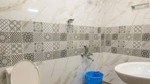 A bathroom with a toilet, a sink, and a blue bucket on the floor. - Raj Sea Front Beach Resort 203 (Mangaluru)