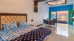 A bedroom with a large bed, a desk, and a view of the sea. - Raj Sea Front Beach Resort 203 (Mangaluru)