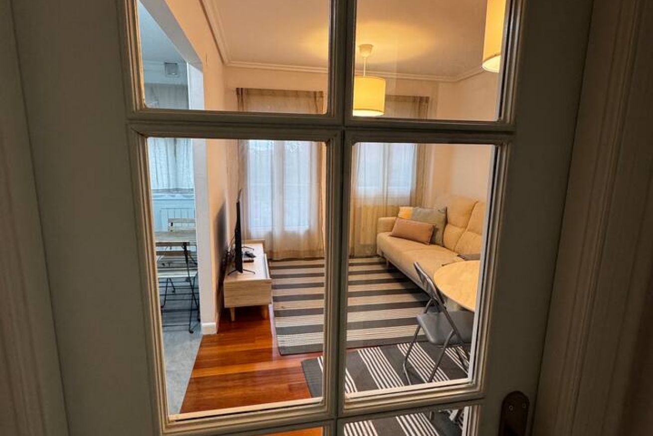 Habitació amb un sofà, una taula petita, una làmpada i vista per la finestra.