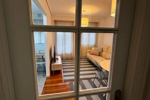 A room with a sofa, a small table, a lamp, and a view through a window.