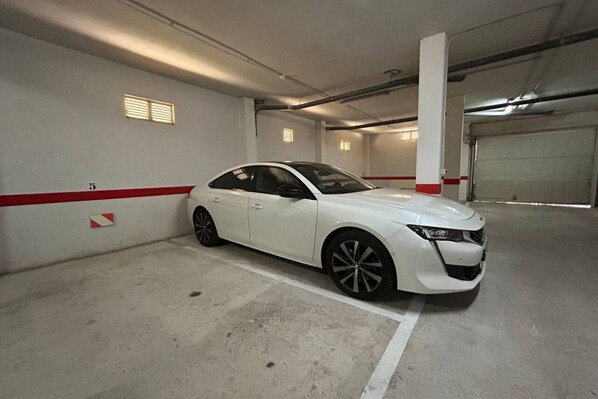 A white car parked in an indoor parking garage with concrete floors and white walls.