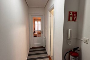 A hallway with a striped carpet, a white door, a fire extinguisher, and a fire alarm on the wall.