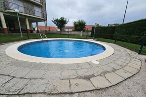 A circular swimming pool with a stone border, surrounded by a fence and a building with a balcony.