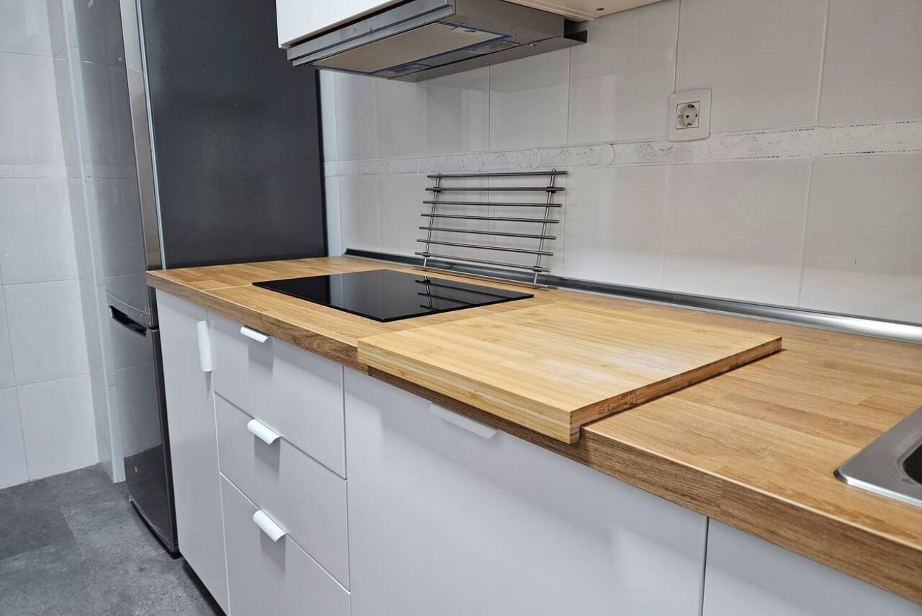 Uma cozinha moderna com bancada de madeira, forno embutido e armários brancos.