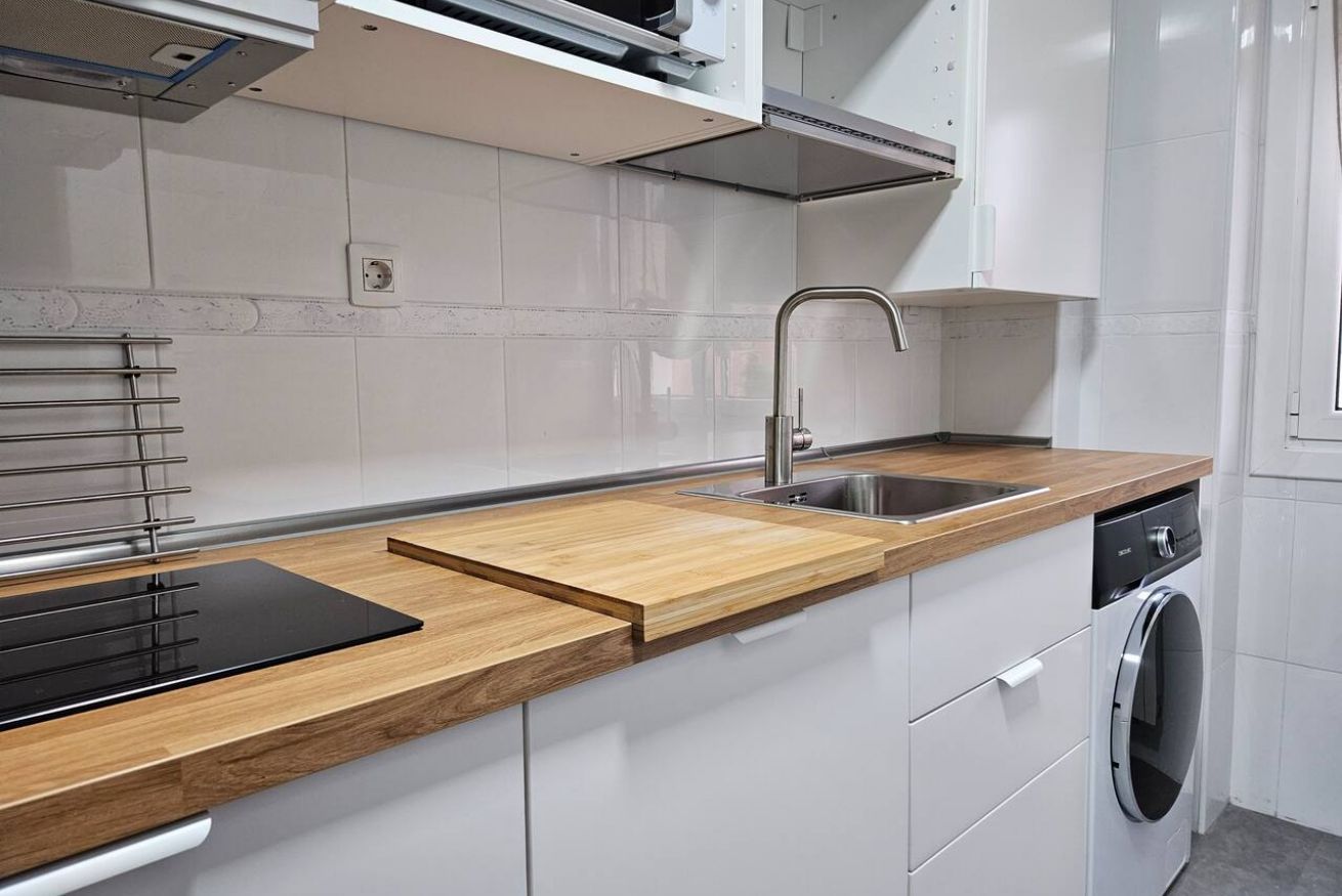 A modern kitchen with a wooden countertop, stainless steel sink, and built-in dishwasher.