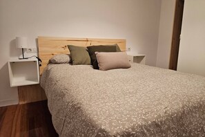 A bedroom with a wooden headboard, a patterned bedspread, two bedside tables with lamps, and a nightstand.