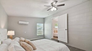 A bedroom with a bed, a ceiling fan, an air conditioning unit, a window with blinds, and a door leading to another room. - Charming Dade City Home with Fire Pit & Garden (Dade City)