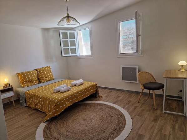 Un dormitorio con cama, mesita de noche, silla, escritorio y ventana.