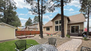 A patio area with a round metal table and chairs, surrounded by a brick walkway and a wooden fence. - Amythist (Flagstaff)