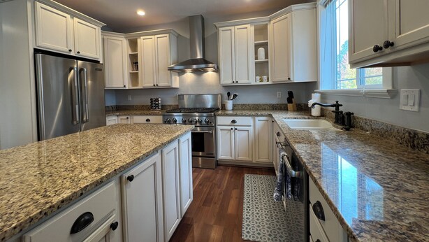 A modern kitchen with white cabinetry, granite countertops, stainless steel appliances, and a large window providing natural light. - Amythist (Flagstaff)