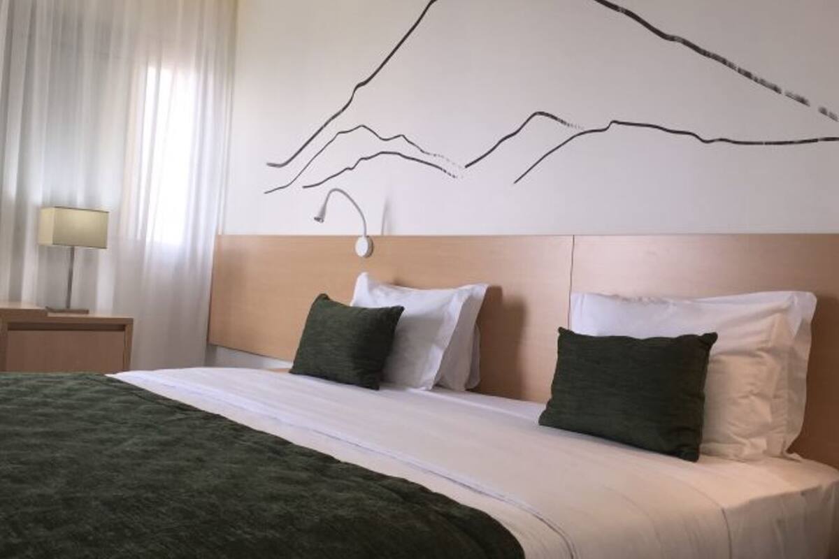 A hotel room with a bed, a nightstand, a lamp, and a wall art piece.