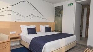A modern hotel room with a large bed, a wooden headboard, and a mountain mural on the wall. - Happy Day Hotel (Praia)
