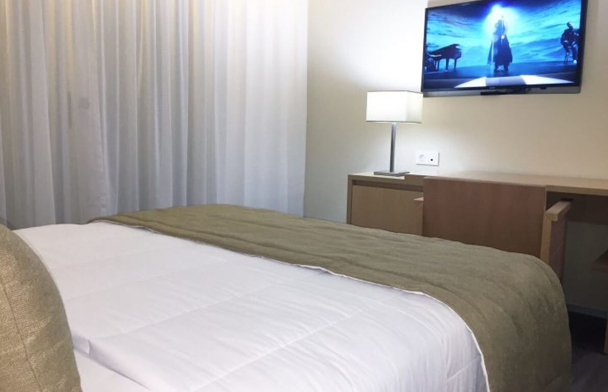 Une chambre d’hôtel avec un lit, un téléviseur fixé au mur, un bureau et une lampe.