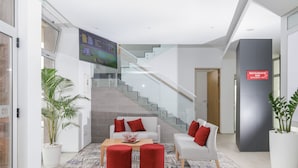 A modern lobby with a staircase, seating area, and a sign for a restaurant/bar. - Happy Day Hotel (Praia)
