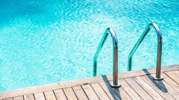 A wooden deck with metal poolside railings leading into a clear blue pool. - Happy Day Hotel (Praia)