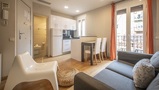 A compact living space with a kitchenette, dining area, and a balcony with orange curtains. - 2 bed apartment in Barceloneta steps from the beach (Barcelona)