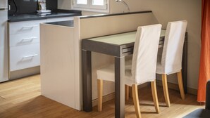 A compact kitchen with a dining area, featuring a small table and two chairs, a countertop, and a cabinet with drawers. - 2 bed apartment in Barceloneta steps from the beach (Barcelona)