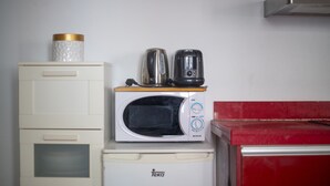 A compact kitchen with a microwave and two coffee makers on a small white appliance, a white cabinet with drawers, and a red countertop.