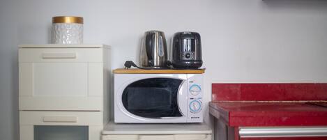 A compact kitchenette with a microwave, kettle, and coffee maker on a small white appliance.