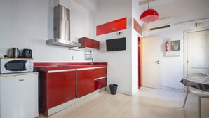 A compact kitchen with a microwave, toaster, and red cabinets. A small trash bin is visible near the sink.