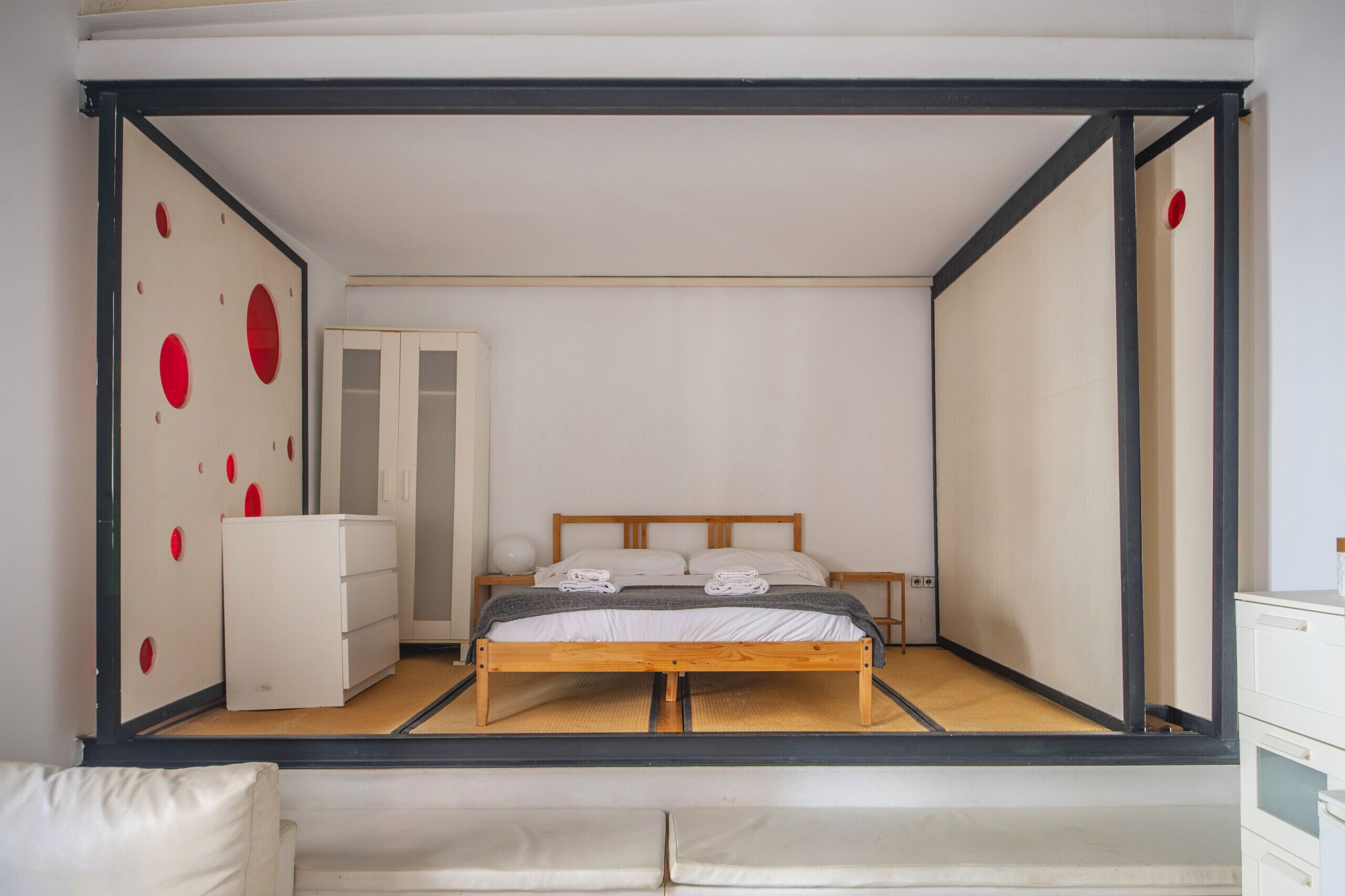 Camera da letto minimalista con un letto, comodini, un armadio e una parete decorata con motivi circolari rossi.