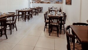 Un restaurante con varias mesas y sillas de madera, paredes blancas y un mural grande con escenas costeras en la pared de fondo.