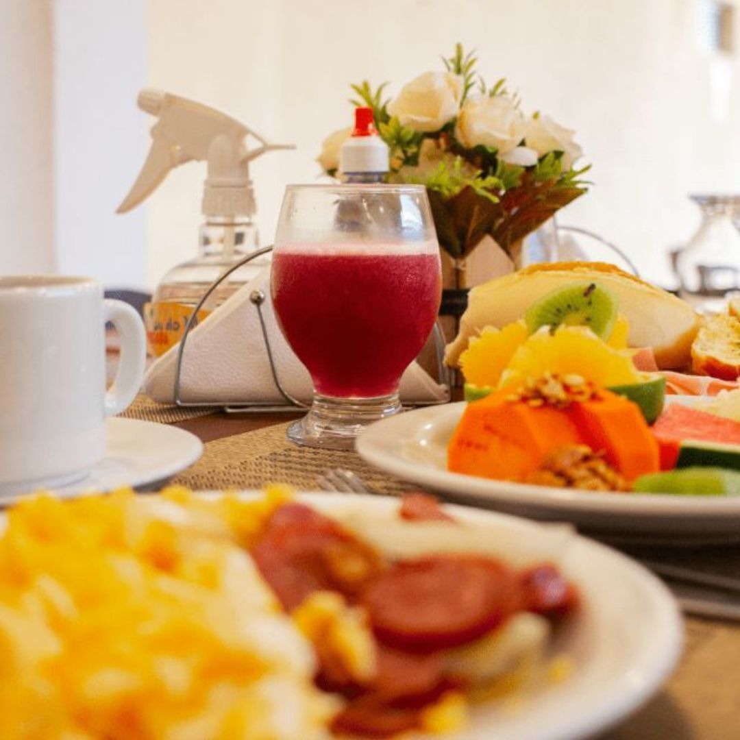 A breakfast table with a glass of red juice, a plate of fruit, a cup of coffee, and a spray bottle.