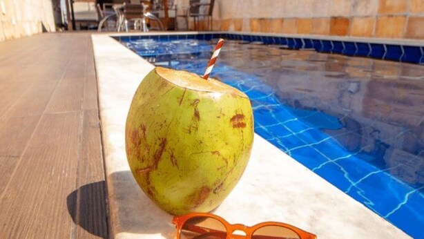 Escena junto a la piscina con un coco y gafas de sol sobre una superficie de mármol.