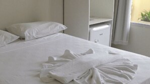 Una cama bien hecha con una toalla doblada y una manta cuidadosamente doblada sobre un edredón blanco.