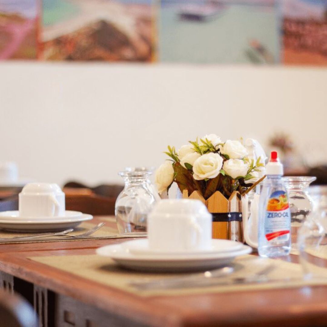 A dining table set with white plates, a clear glass pitcher, a bottle of Zero Cal, and a vase with white flowers.