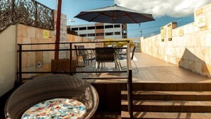 Una terraza en la azotea con zona de comedor, una silla de mimbre y vistas a un edificio al fondo.