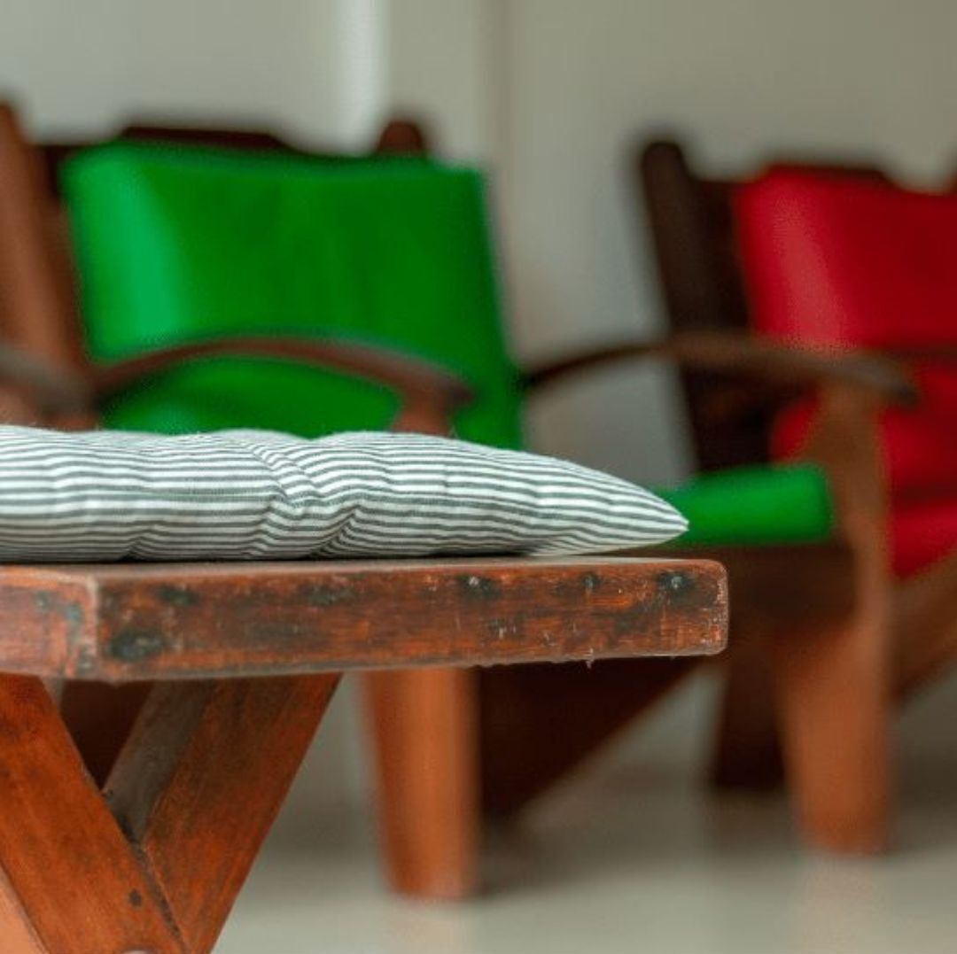 A wooden table with a striped pillow on it, surrounded by chairs with green and red cushions.