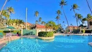 A clear blue swimming pool with a tiled edge, surrounded by palm trees and lounge chairs. - Carey Beach Villa at Palmas del Mar (Palmas del Mar)