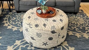 A living room with a grey sofa, striped pillows, a round ottoman with a nautical theme, a wall-mounted painting of a sea turtle, and two floor lamps. - Carey Beach Villa at Palmas del Mar (Palmas del Mar)