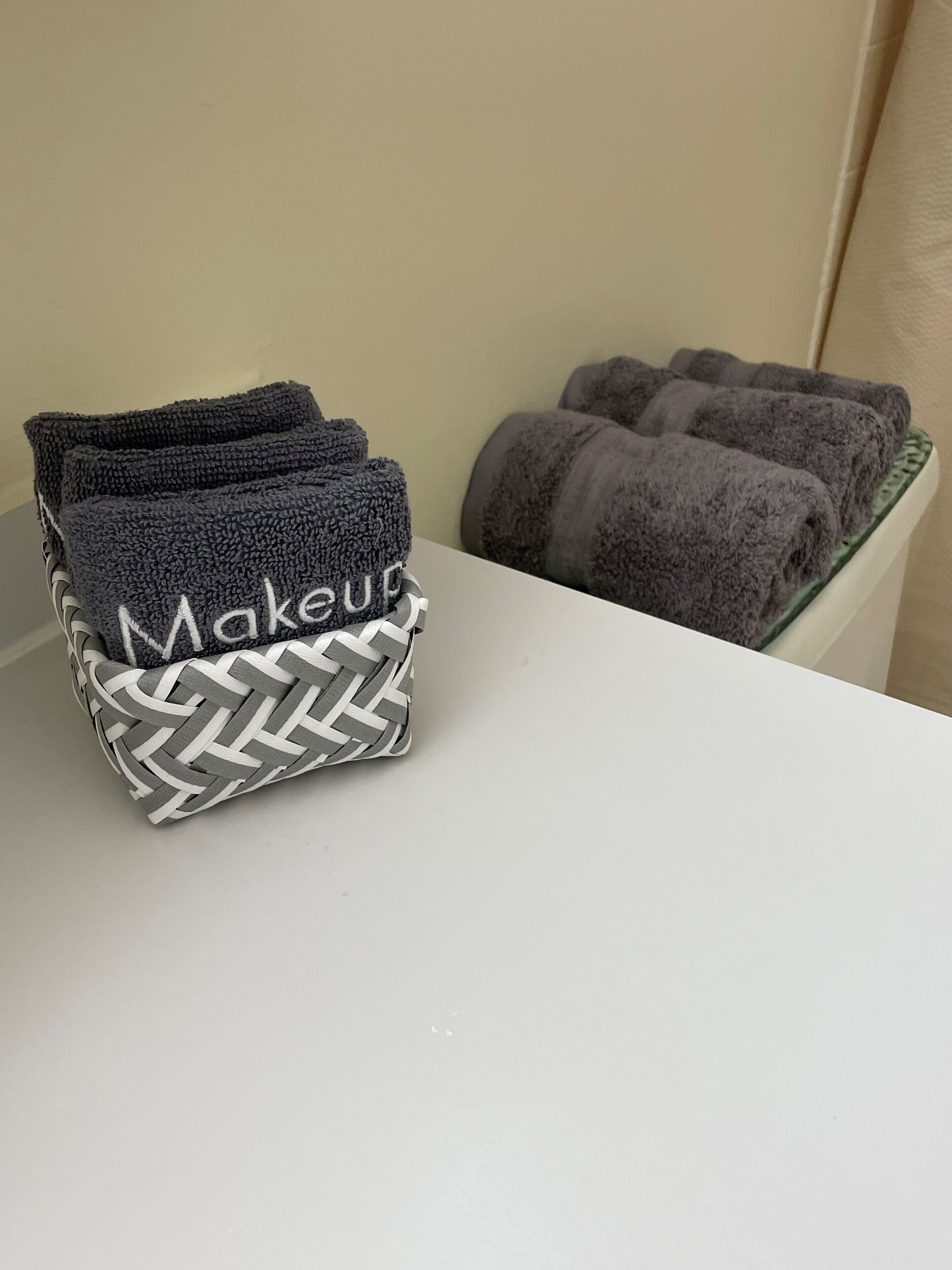 A white table with a woven basket containing folded towels and a stack of rolled towels.