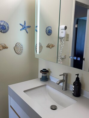 Une salle de bain avec un lavabo blanc, un miroir et des coquillages décoratifs accrochés au mur.