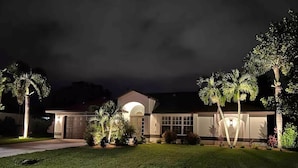 A residential house with a well-maintained lawn, a garage, and palm trees.