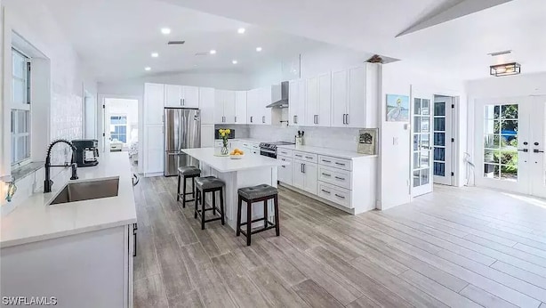 A modern kitchen with white cabinets, a central island with stools, a refrigerator, and a coffee maker.