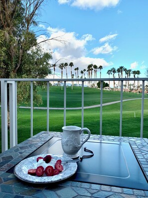 Una mesa con un plato de fresas y una jarra blanca, con vista a un campo de golf con palmeras.