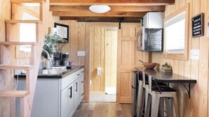 A compact kitchen with a wooden interior, a microwave, a sink, and a bar stool area. - Tiny Home Sleep 4 PALO DURO CANYON Base Camp WTAMU (Canyon)