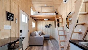 A compact, wooden interior with a bunk bed, a sofa, and a kitchen area. - Tiny Home Sleep 4 PALO DURO CANYON Base Camp WTAMU (Canyon)