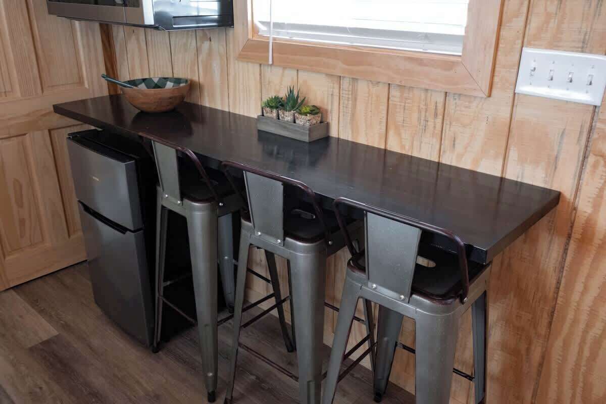 A kitchen with a dark countertop, four bar stools, a small wooden bowl, and a planter with succulents.