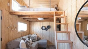 A compact, wooden interior with a sofa, a ladder, and a circular mirror. - Tiny Home Sleep 4 PALO DURO CANYON Base Camp WTAMU (Canyon)