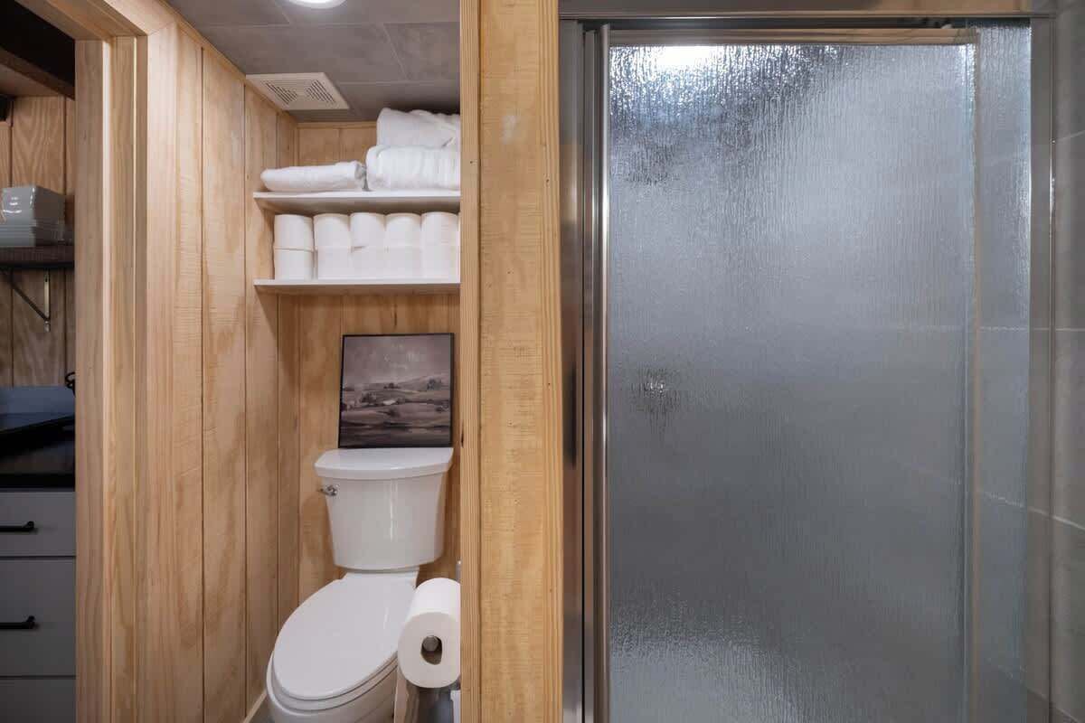 Un bagno compatto con il water, uno scaffale con asciugamani e un quadro appeso al muro.