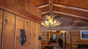 A wooden interior with a chandelier, a door with a bear emblem, and a hallway leading to a dining area.
