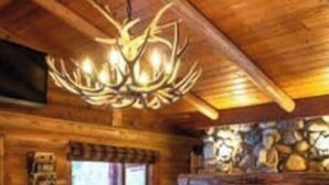 A cozy log cabin interior with a stone fireplace, wooden furniture, and a chandelier.