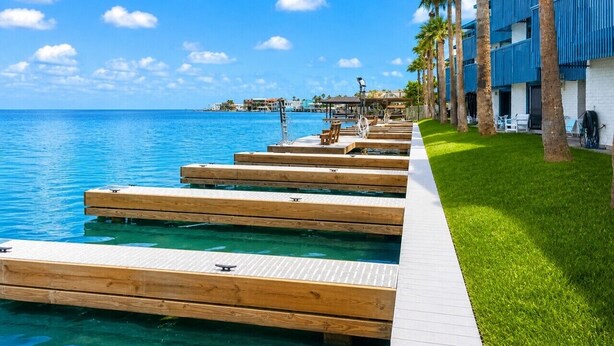 A waterfront hotel with wooden docks, palm trees, and a clear blue sky. - Las Brisas on the Bay Unit 119 (South Padre Island)