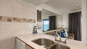 A modern kitchen with a double sink, a dishwasher, and a large mirror above the sink. - Las Brisas on the Bay Unit 119 (South Padre Island)