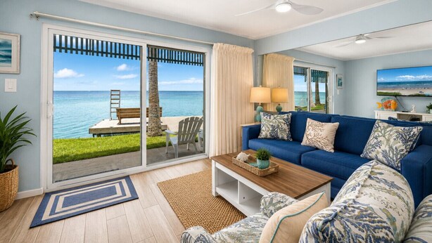 A room with a blue sofa, a coffee table, and a view of the ocean through a sliding glass door. - Las Brisas on the Bay Unit 116 (South Padre Island)