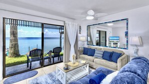 Een woonkamer met een grote schuifpui die uitkomt op een balkon met uitzicht op zee. Er is een bank, een salontafel en een televisie.